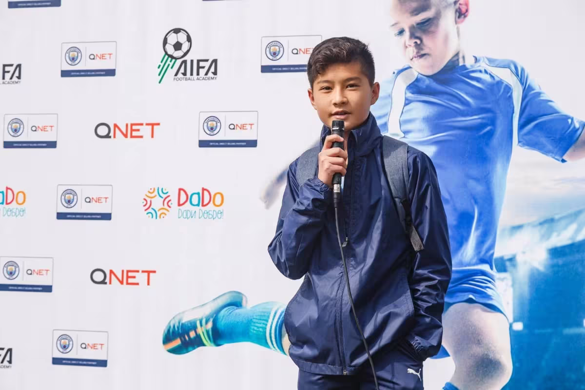 Qnet Football Tournament For Children A Grand Success 2 student from QNET-City football language school during an interview QNET man city backdrop