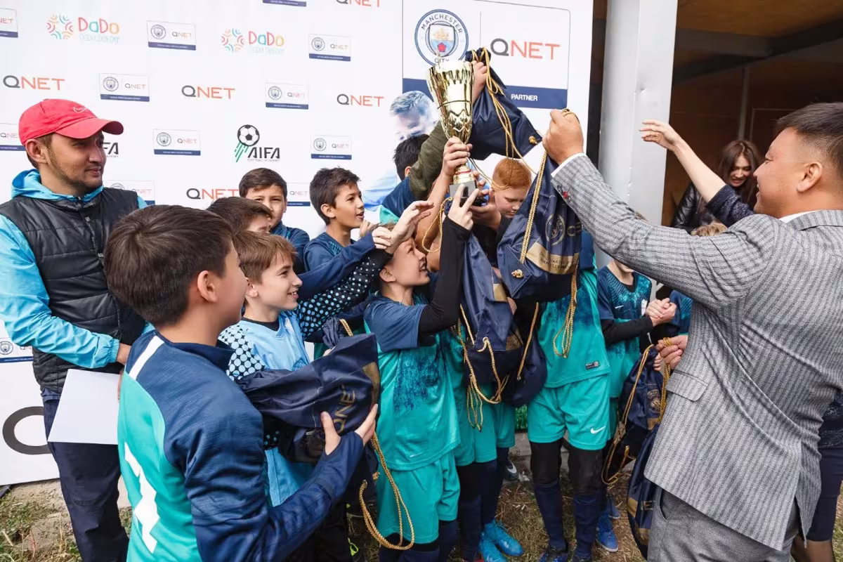 Qnet Football Tournament For Children A Grand Success 4 Children celebrating holding trophy in air and QNET-city bags.