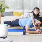 A father doing push-ups with his delighted daughter on his back in the living room, featuring HomePure bottle and HomePure for cleanliness.