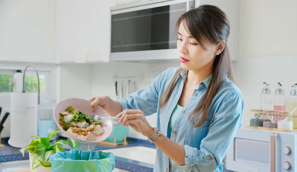 8 Tips And Tricks For Reducing Food Waste At Home 2 A woman throws leftover food into the trash, creating a food waste problem at home.