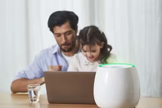 A father and his daughter sit at a table with a laptop, while HomePure Zayn ensures safe and clean indoor air