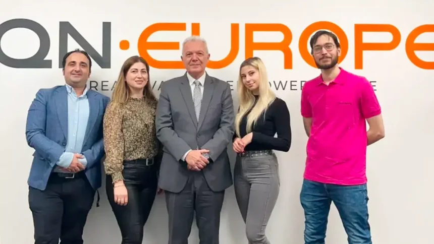 QN Europe Team posing in front of company logo on the wall