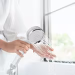 Hand holding a HomePure Rayn shower head with flowing water