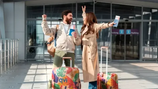 couple outside airport cheering with their luggage