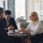 Woman mentoring two men in business leadership over coffee
